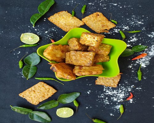 Traditional Indonesian food served on a wooden table with tempeh, vegetables, and rice
